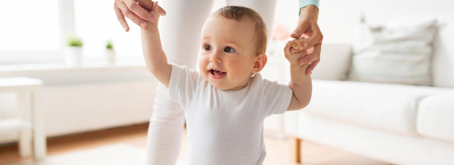 Bebê branco tentando andar com o auxílio de uma mulher Bebê branco tentando andar com o auxílio de uma mulher